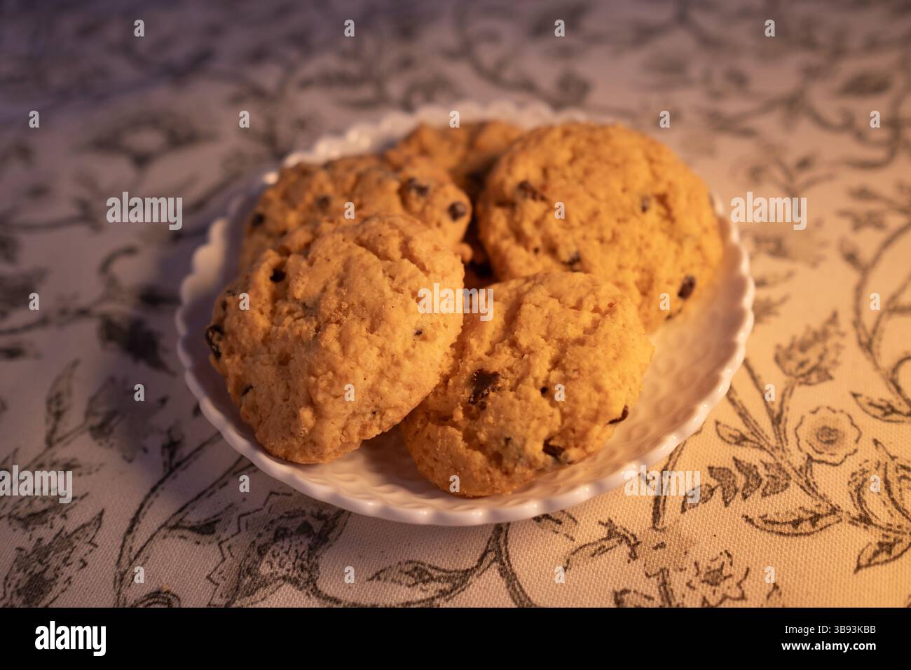 Small wicker plate with five delicious chocolate chips gluten free cookies. They are fresh, baked and handmade. The dish is placed on a classic floral Stock Photo