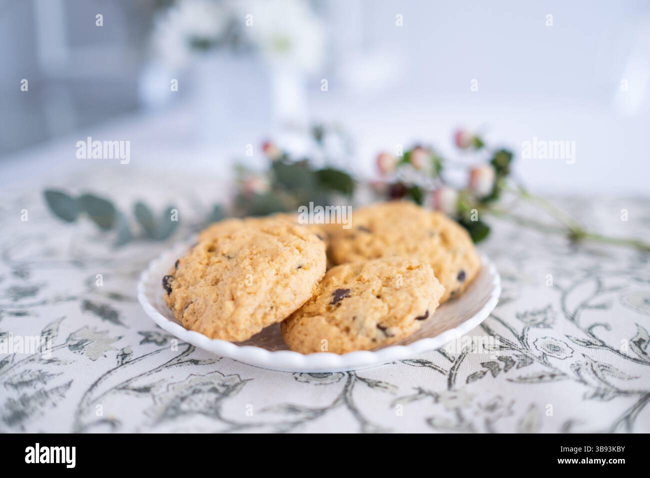 Small wicker plate with some delicious chocolate chips gluten free cookies decorated with flowers. They are fresh, baked and handmade. The dish is pla Stock Photo