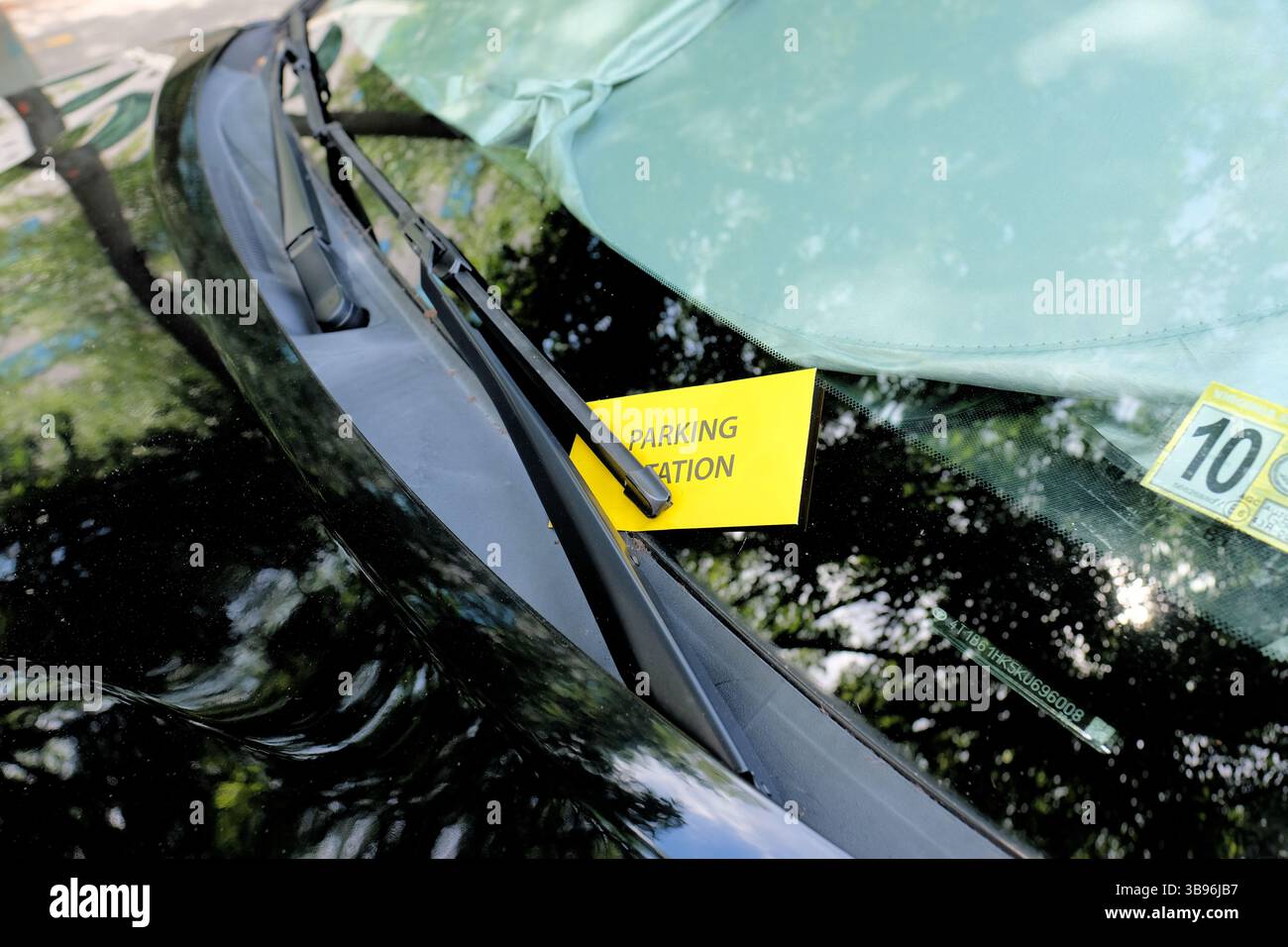 A yellow parking citation envelope under a black car's windshield wiper containing a ticket for a parking violation in downtown Richmond, Virginia. Stock Photo