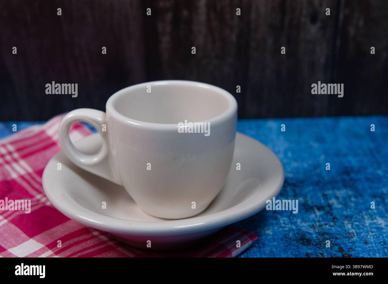 A white ceramic cup and saucer on blue with a red and white linen napkin. Stock Photo