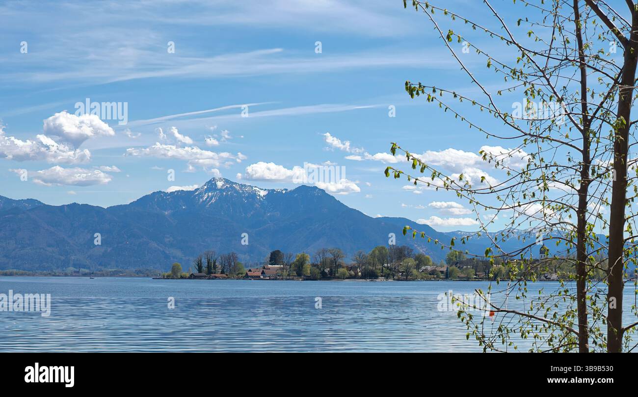 A springtime view of Fraueninsel on Lake Chiemsee framed by a tree and a wooden pier. Stock Photo
