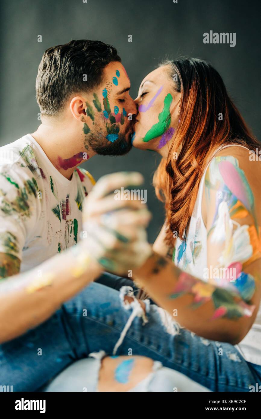 Color-splattered couple kisses while holding hands during paint play Stock Photo