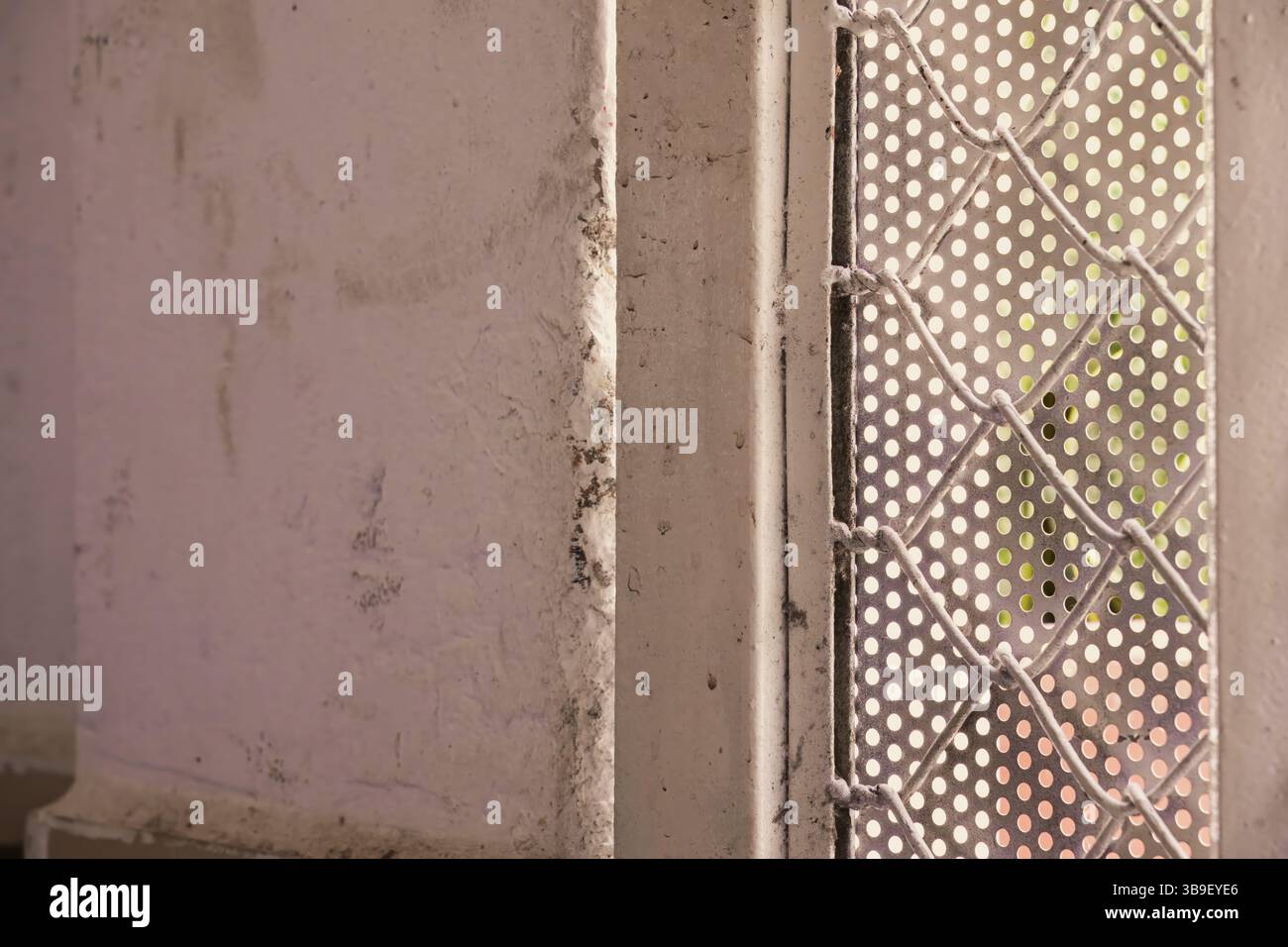 Close up of a weathered white wall next to a perforated metal sheet Stock Photo