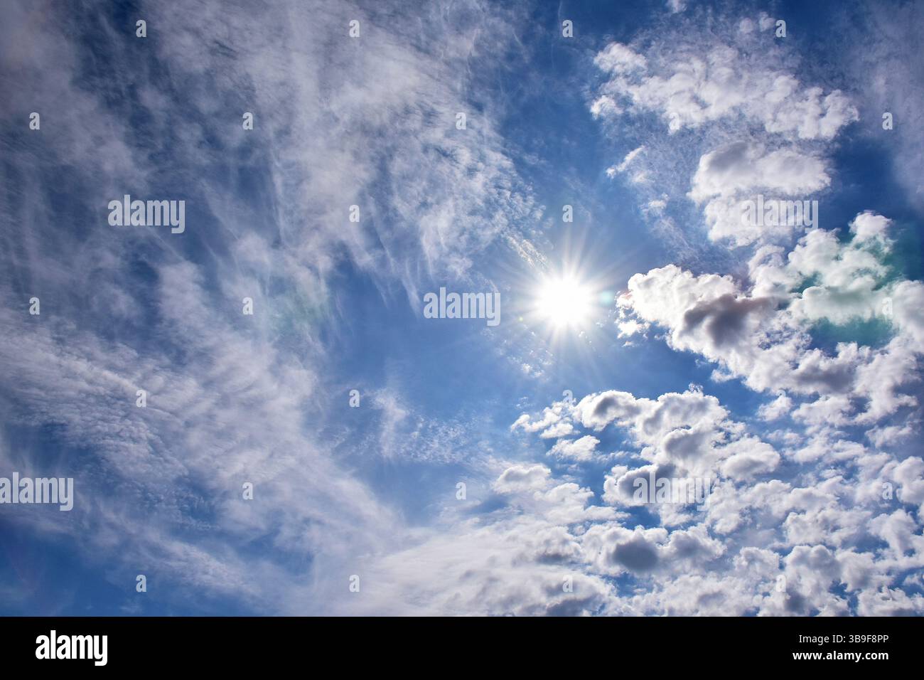 Bright sun between cirrus and cumulus clouds Stock Photo