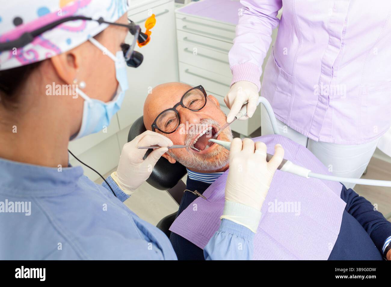 Dentist wearing magnifying glasses performing a dental checkup on ...