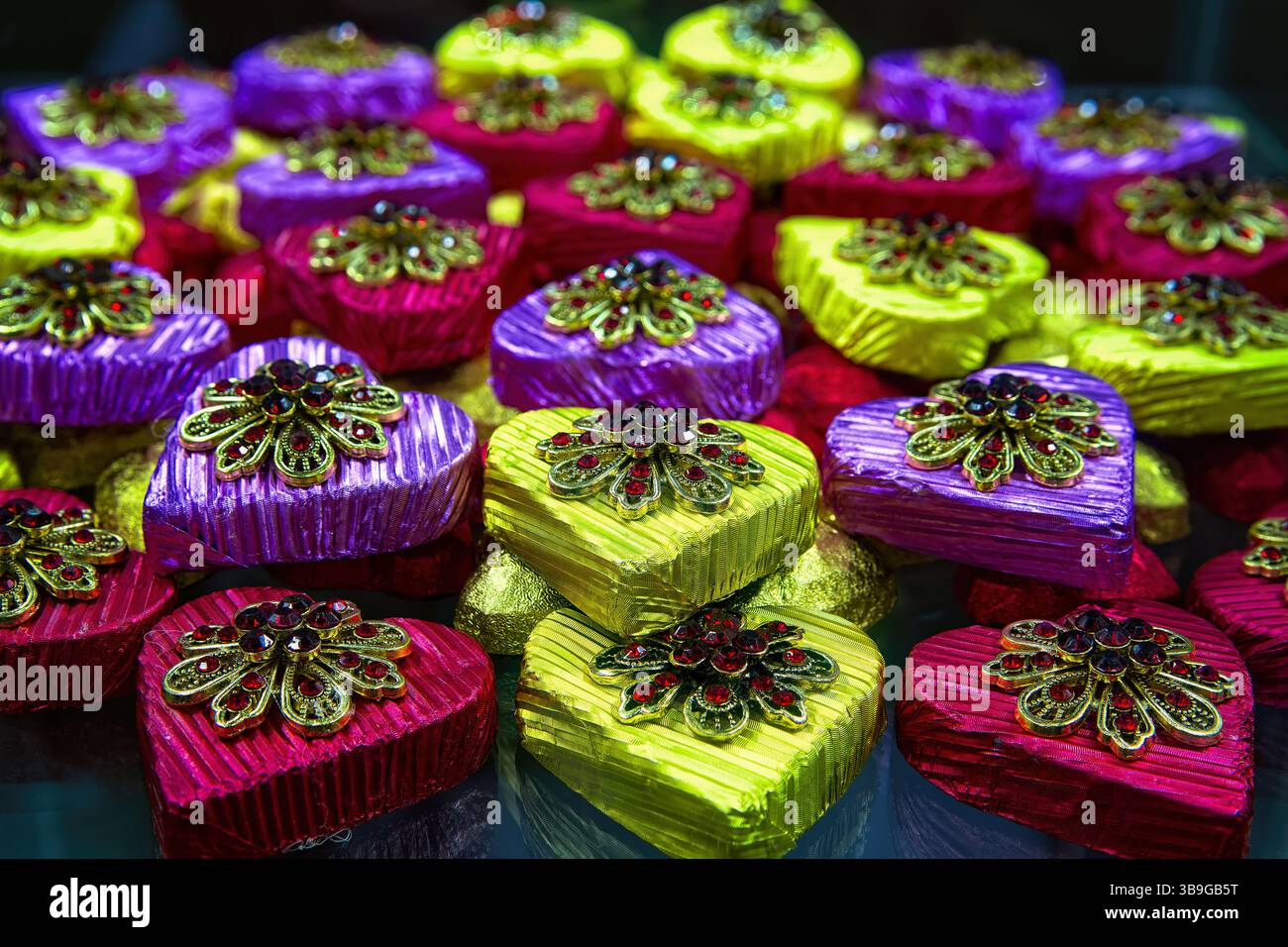 Multicolored chocolate candies in the shape of heart in shiny wrapper with gift brooch, top view. Stock Photo