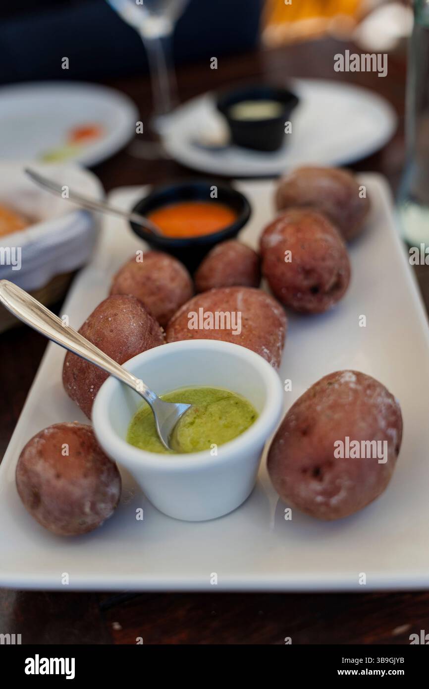 The typical Canarian dish papas arrugadas, crumbly boiled potatoes with green and red sauce (mojo rojo and mojo verde) is served on a plate. Canarian potatoes with a salt crust. Stock Photo