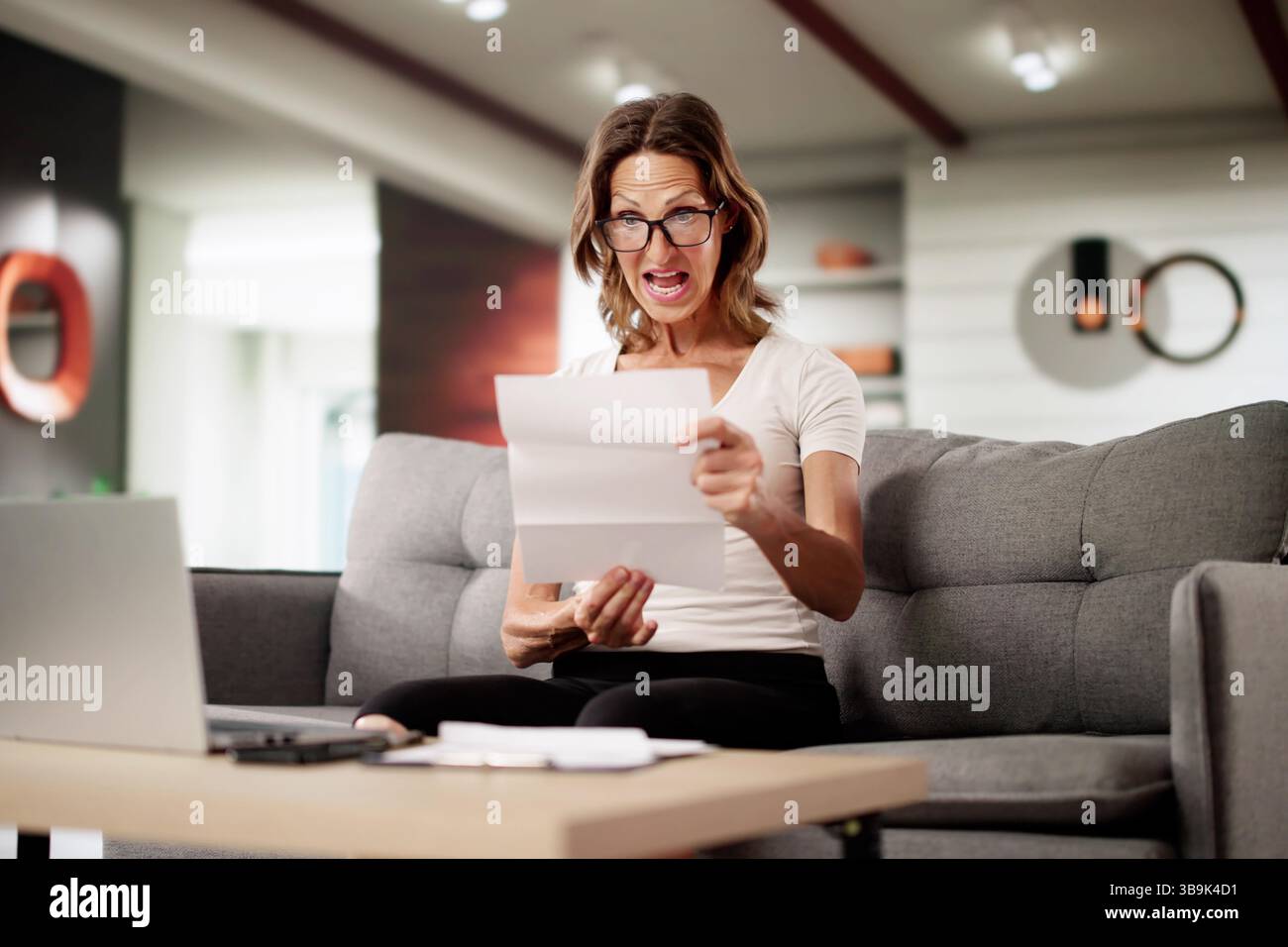 Troubled Accountant Reviewing Shocking Invoice On Laptop, Feeling Overwhelmed And Stressed. Stock Photo