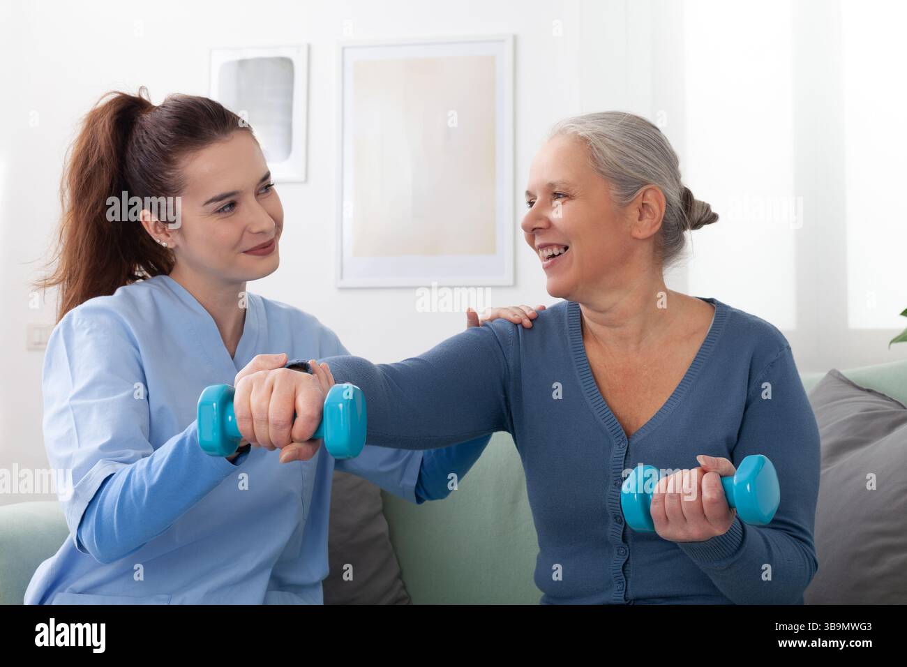Smiling young nurse assisting an elderly woman with light dumbbell ...