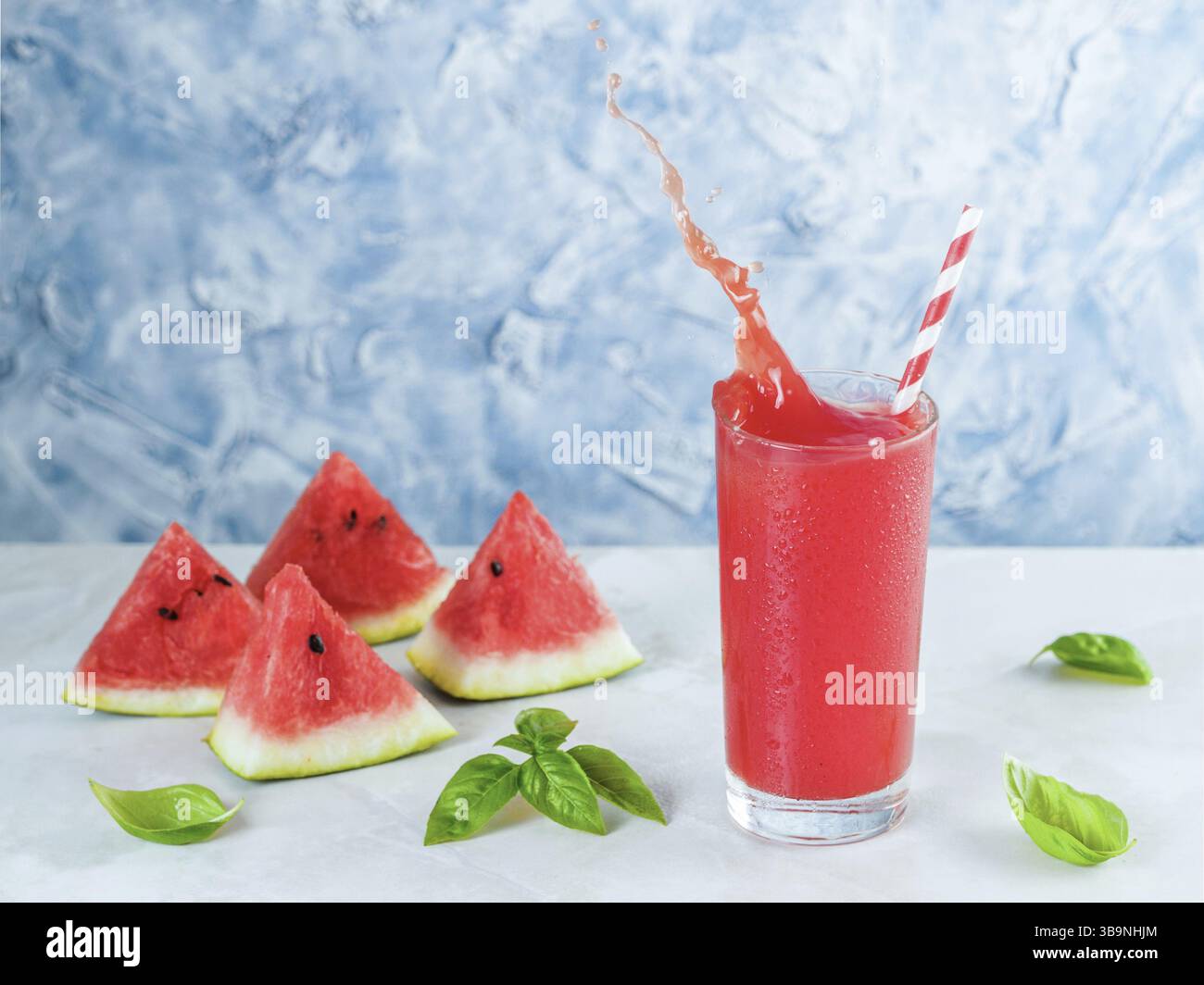 Tasty appetizing watermelon drink with basil in in glass on gray table. Homemade watermelon and basil lemonade with splashes. Copy space. Slice waterm Stock Photo