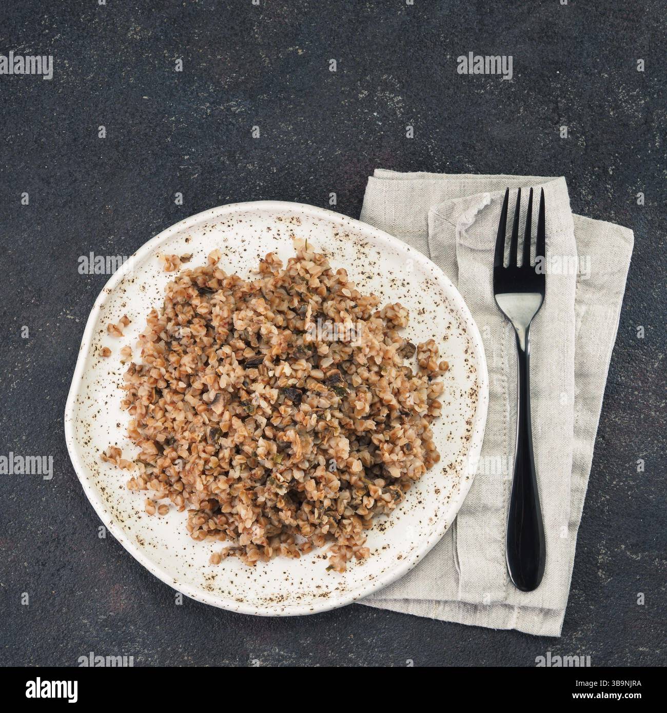 Buckwheat risotto with dried mushrooms in craft plate on black cement background. Gluten-free and vegetarian buckwheat recipe ideas. Copy space. Top v Stock Photo