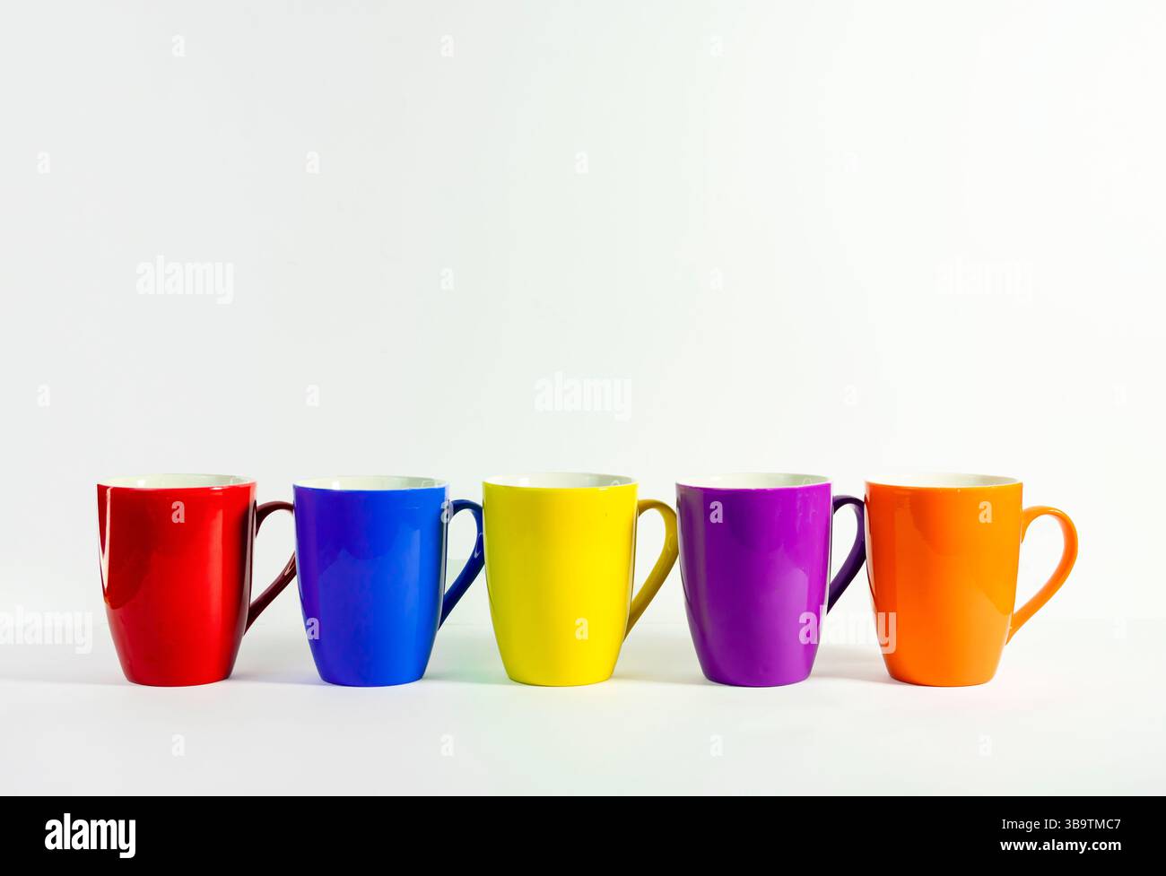 Vibrant coffee mugs stacked on a White minimalistic surface. Fun and Playful Color Cup Arrangement for Modern Product Display On white Background Stock Photo