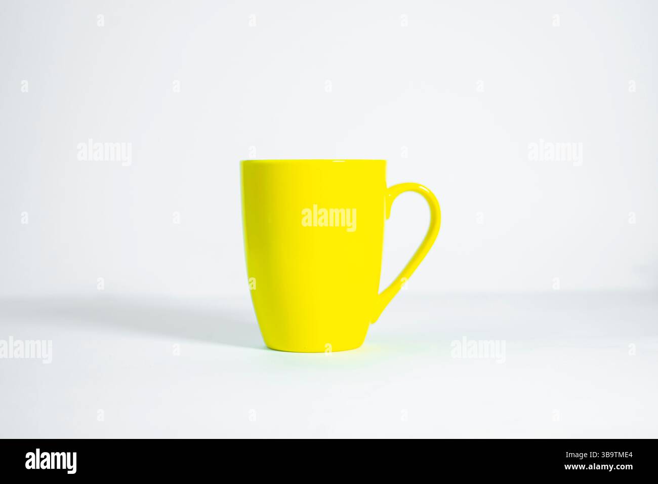 Simple yellow ceramic mug with handle, isolated on smooth white background. Stock Photo