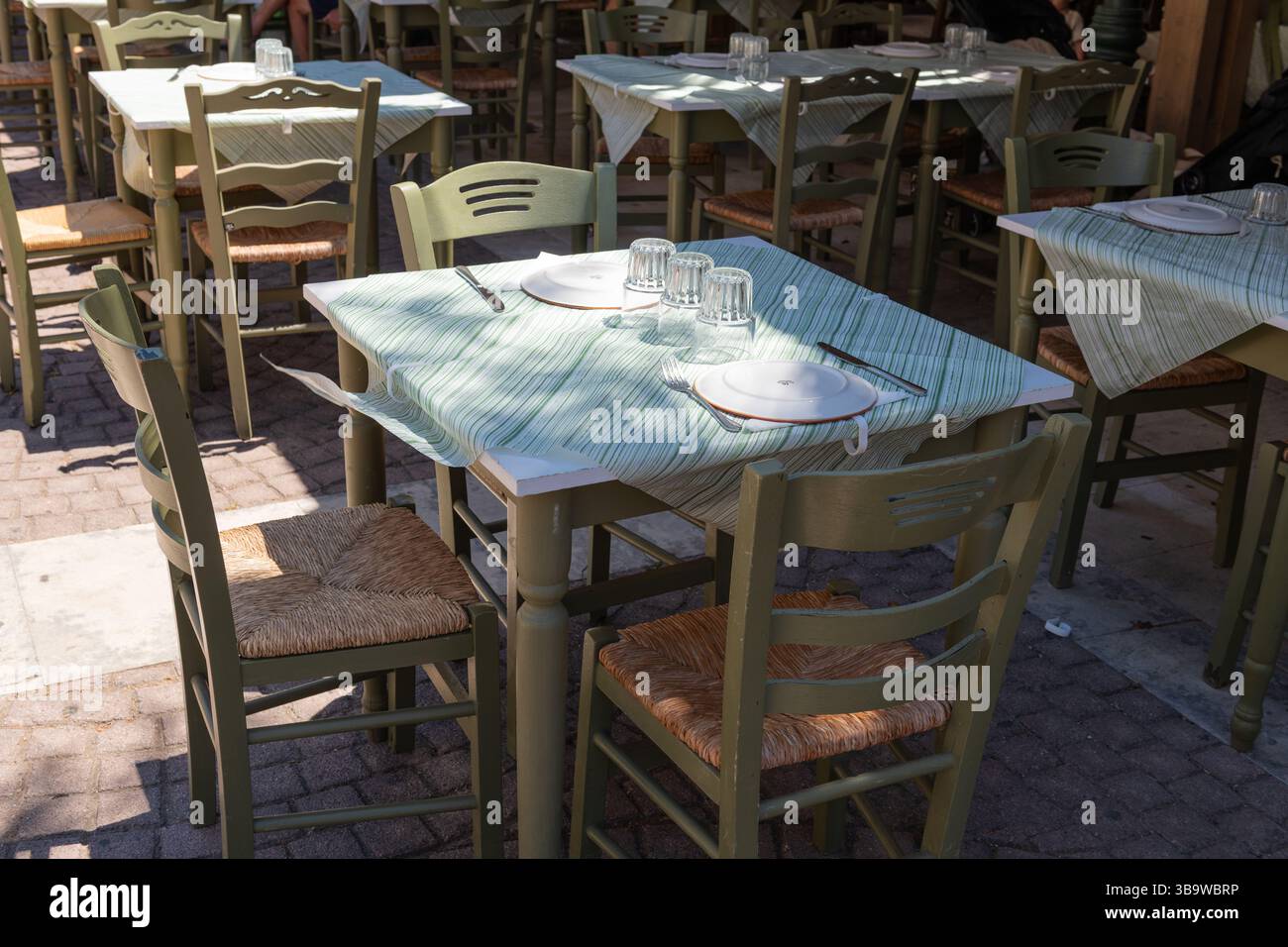 Traditional Greek taverna table set with plates and glassware, shaded ...