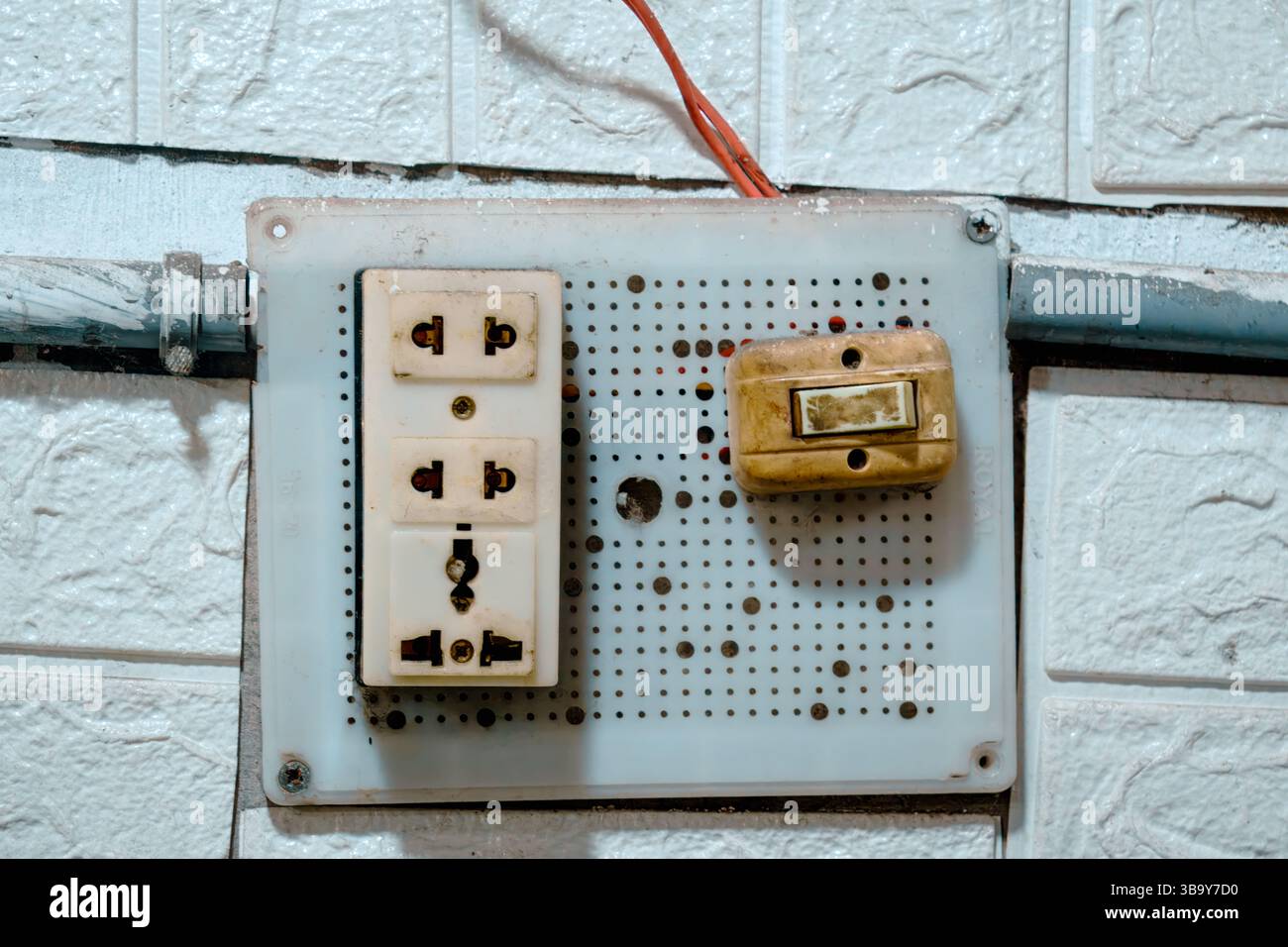 Old electrical switchboard mounted on a tiled wall Stock Photo
