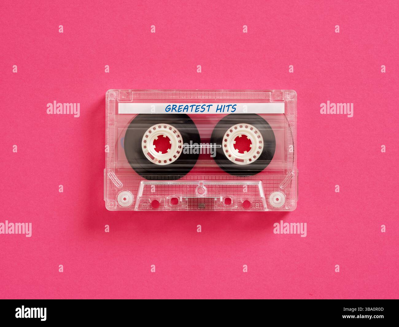 Music greatest hits mix tape concept. Transparent audio cassette tape with greatest hits inscription lying on pink background. Stock Photo