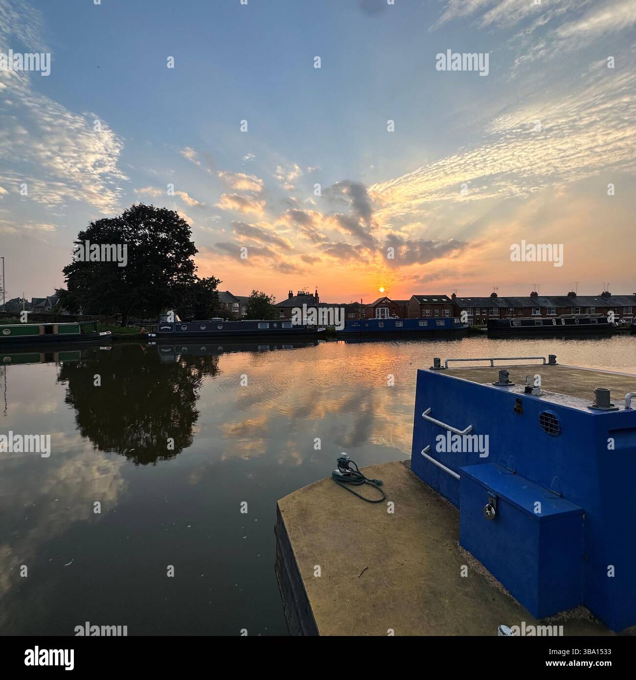 Chester canal at sunset with trees, houses, and fluffy clouds reflected in still water on a clear evening, showing vivid sky and calm reflections. - Smartphone Captured Stock Image