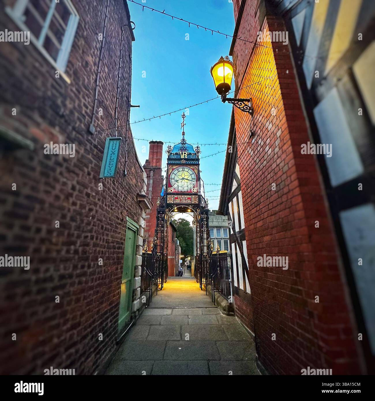 Twilight view of Eastgate Clock, Chester, from city walls looking north, framed between buildings with street lights glowing and blue evening sky - Smartphone Captured Stock Image