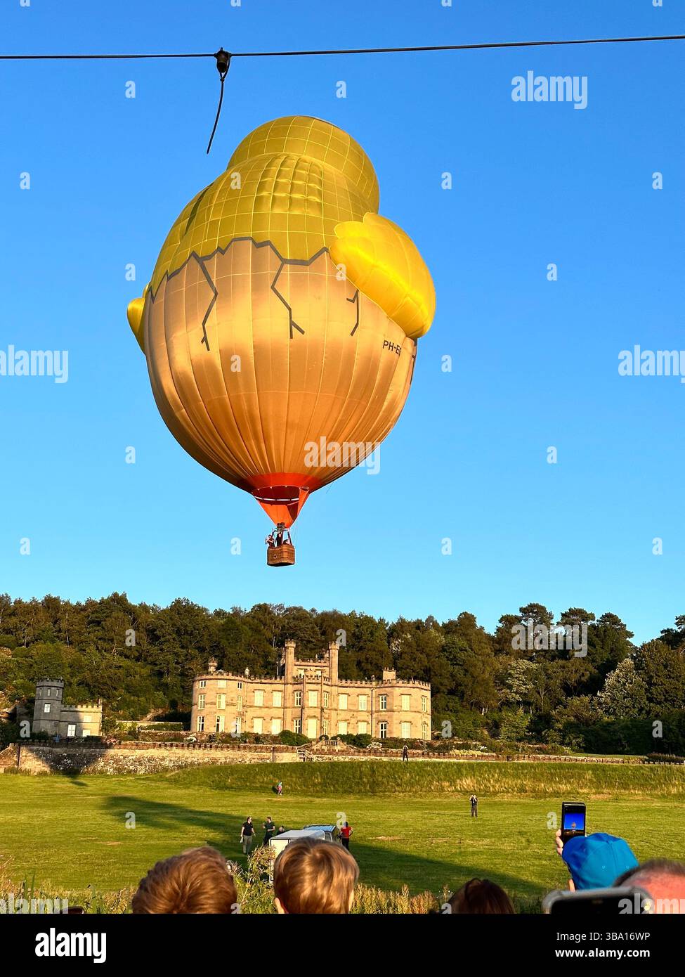 Hot air balloon shaped like a chick hatching from an egg flying above Bolesworth Castle during Cheshire Balloon Fiesta, Tattenhall, UK, 6 August 2023. - Smartphone Captured Stock Image