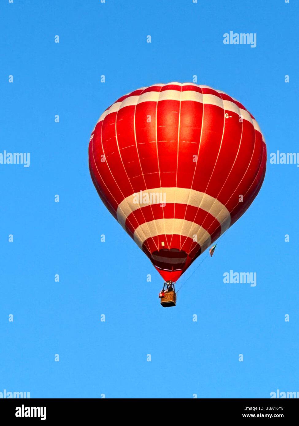 Red and white hot air balloon floating against a clear blue sky during the Cheshire Balloon Fiesta, Tattenhall, UK, 6 August 2023. - Smartphone Captured Stock Image