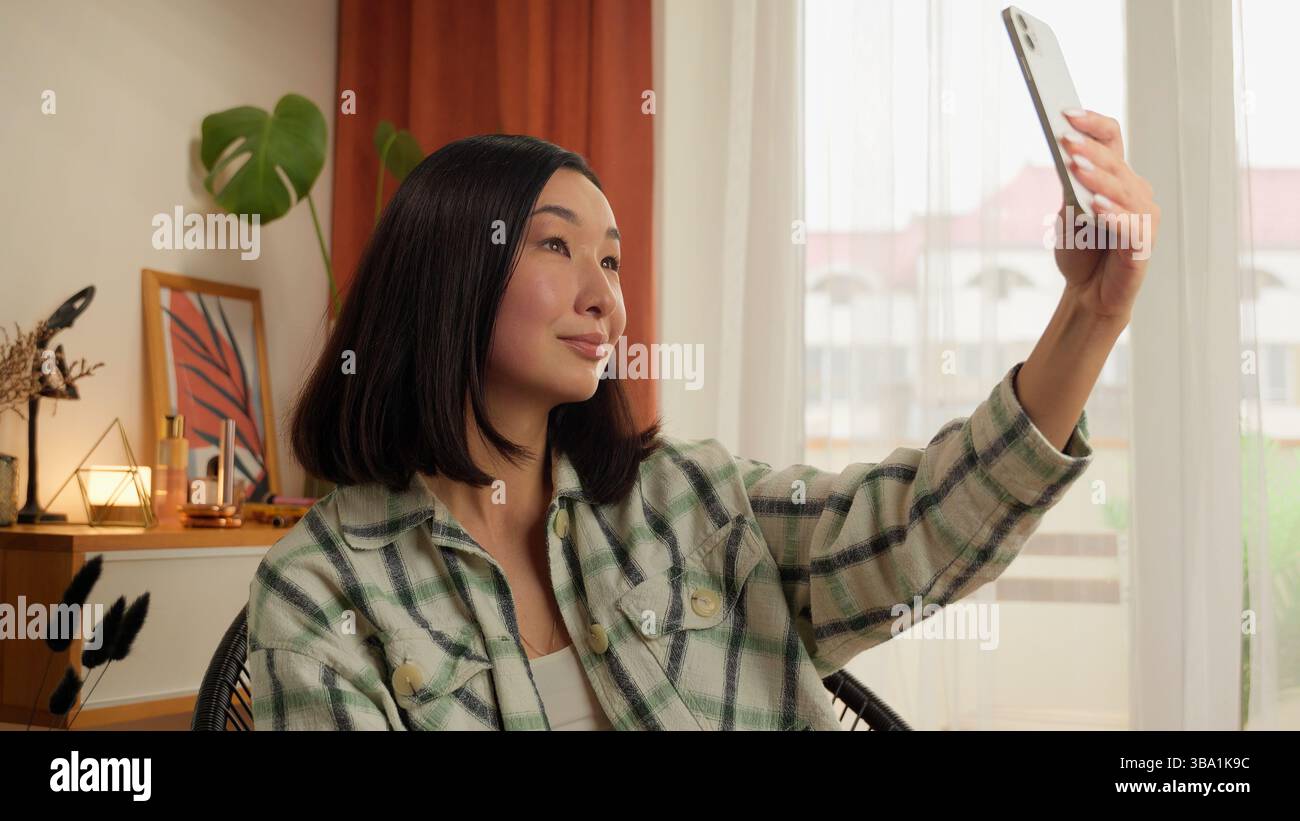 Asian Korean Chinese Japanese woman holding using mobile phone smartphone female girl make photo picture selfie web camera posing blogger influencer Stock Photo