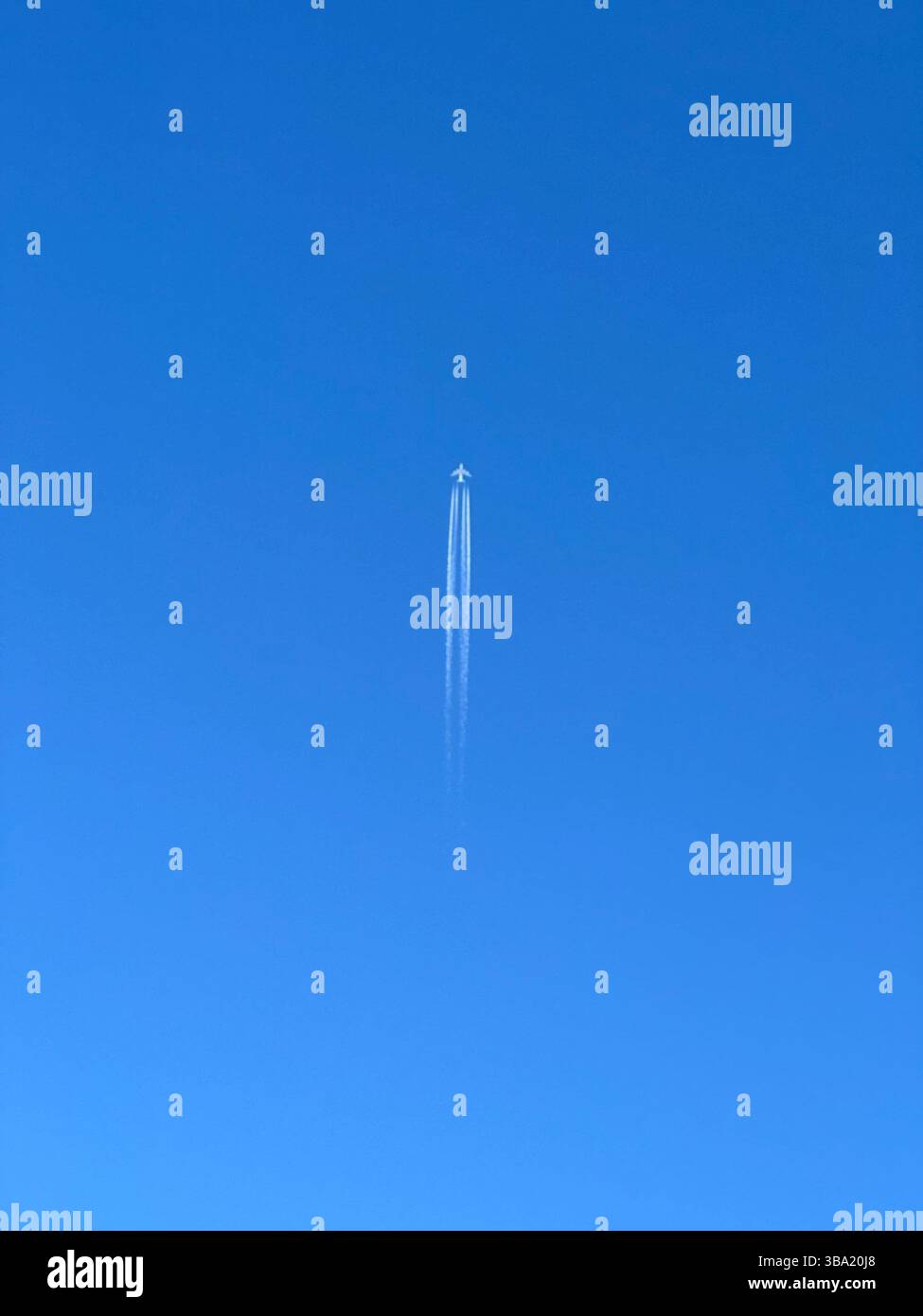 An airplane streaks across a bright blue sky, leaving a wispy contrail in its wake. - Smartphone Captured Stock Image An airplane streaks across a bright blue sky, leaving a wispy contrail in its wake. - Smartphone Captured Stock Image