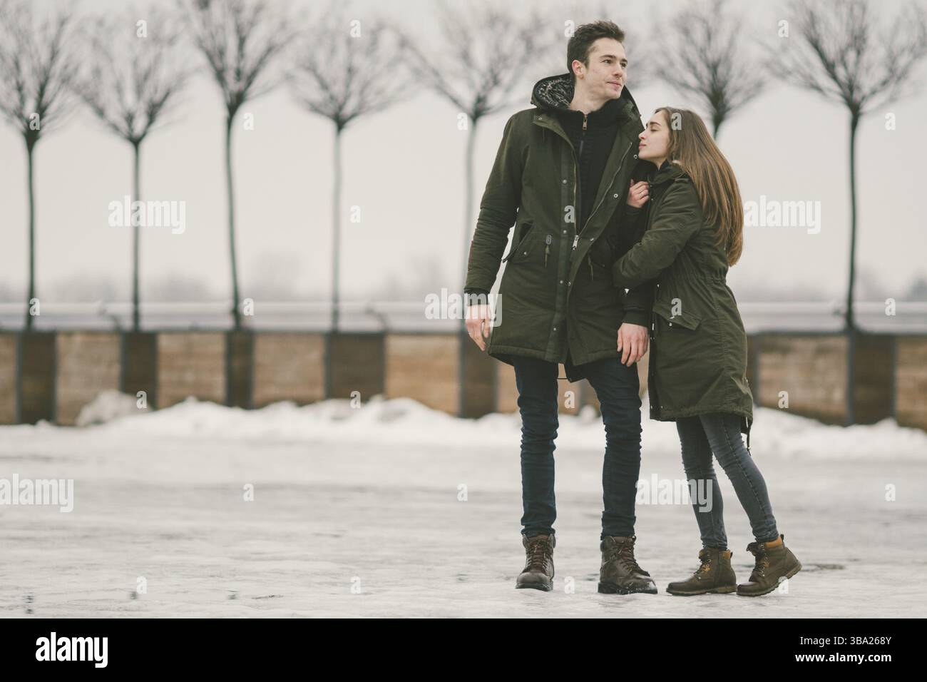 A heterosexual couple young people in love students a man and a Caucasian woman. In winter, in the city square covered with ice, they walk, hug and ki Stock Photo