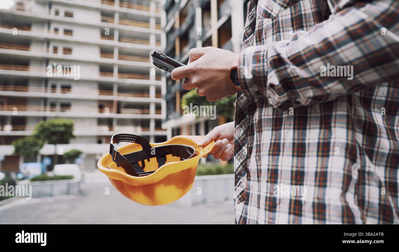 Young Engineer using smartphone on construction site. Architect using phone. Manager development building texting on smart phone. Builder makes notes Stock Photo