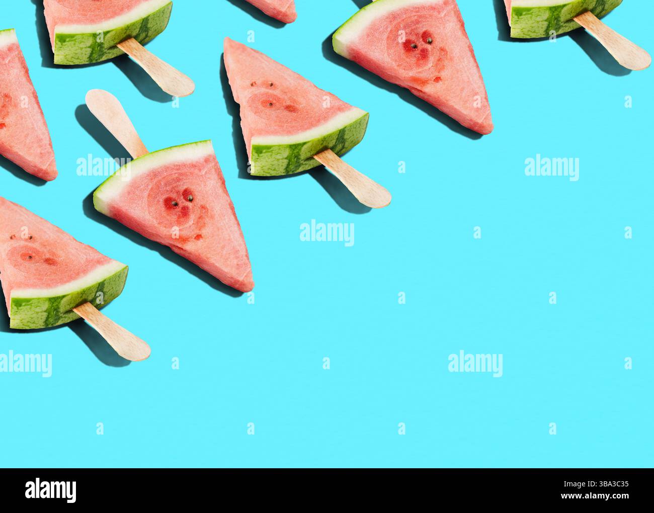 Fresh watermelon wedges with popsicle sticks laid out diagonally on vivid bold blue background, summer refreshing snack, pattern Stock Photo