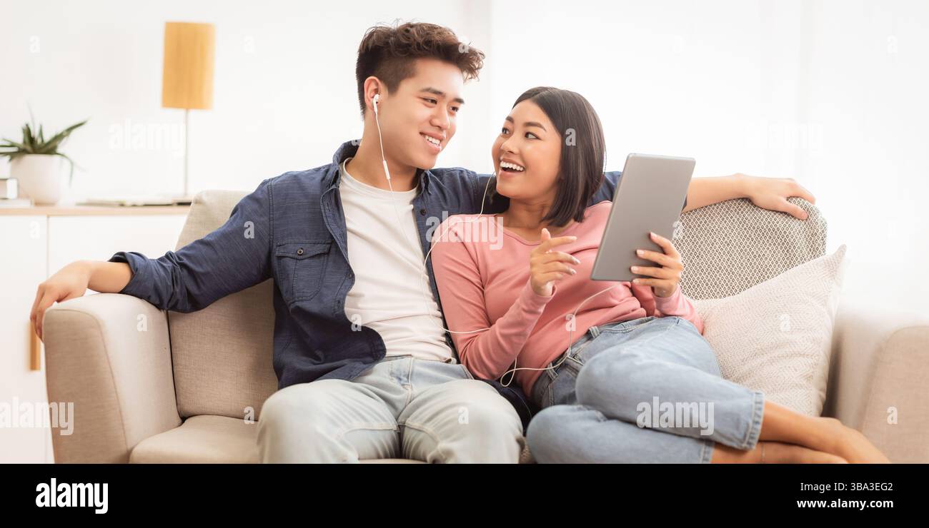 Japanese Spouses Using Tablet Browsing Internet Sitting On Couch Indoor Stock Photo