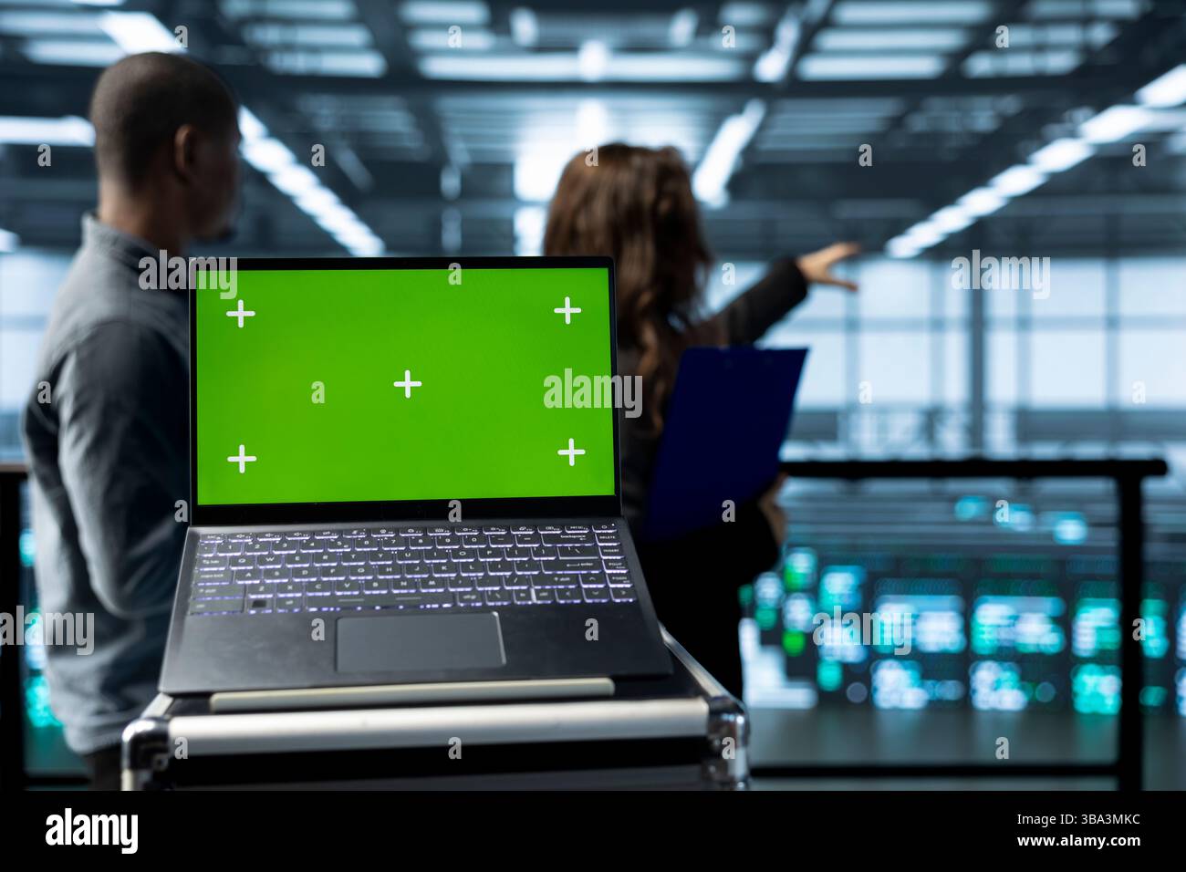 Isolated screen mockup laptop in front of technicians in blurry background supervising server room gear. Close up of chroma key notebook next to admins overseeing data center rigs Stock Photo