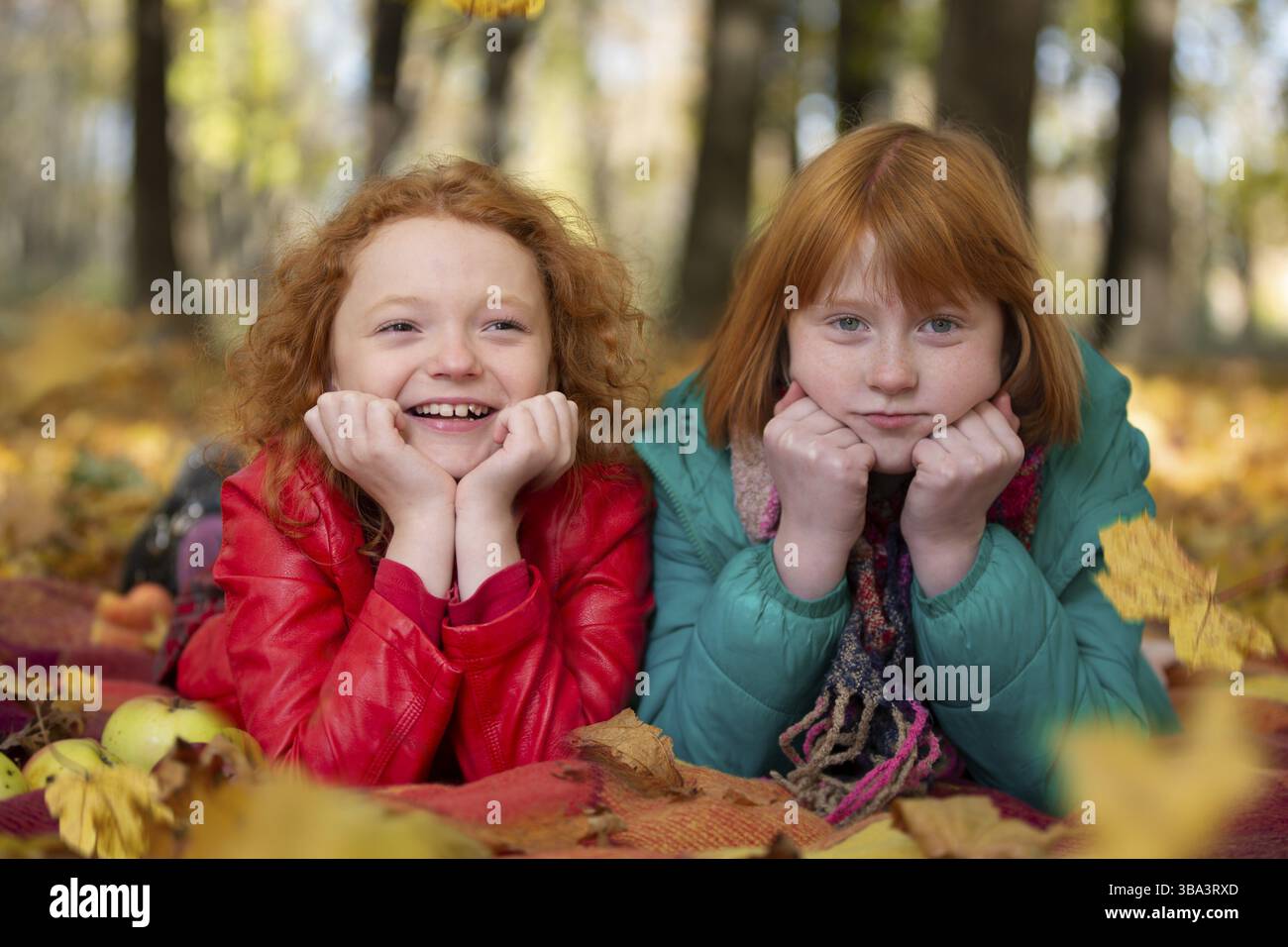 Portrait of two pretty girl sisters lying on the leaves in the autumn park Stock Photo