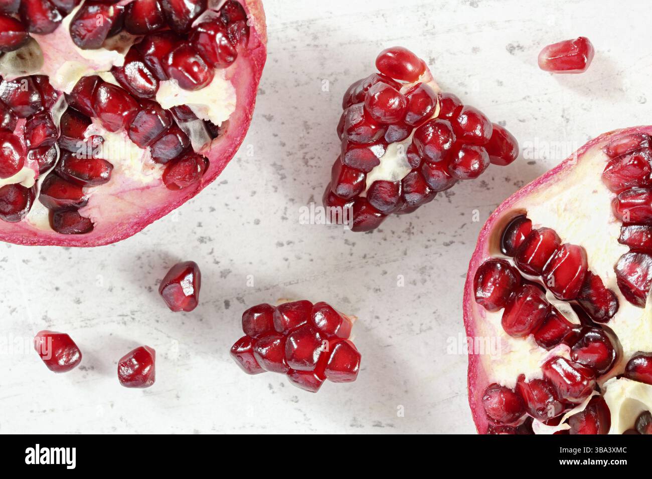 Tabletop closeup view - pomegranate half, clusters of gem like fruits scattered on white board, Liptovsky Hradok, Slovakia, Europe Stock Photo