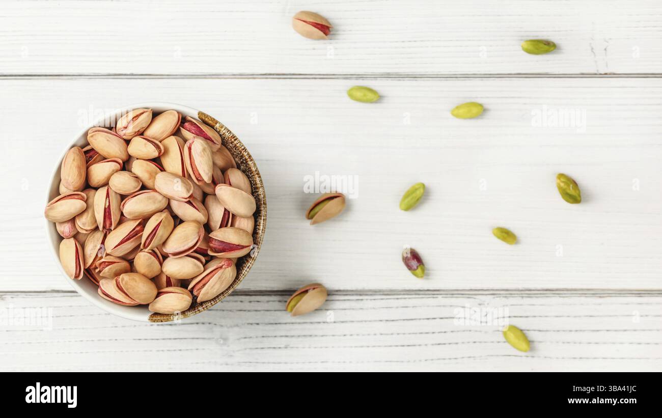Tabletop view, small bowl with red Turkish pistachios, more nuts scattered on white board desk, Liptovsky Hradok, Slovakia, Europe Stock Photo