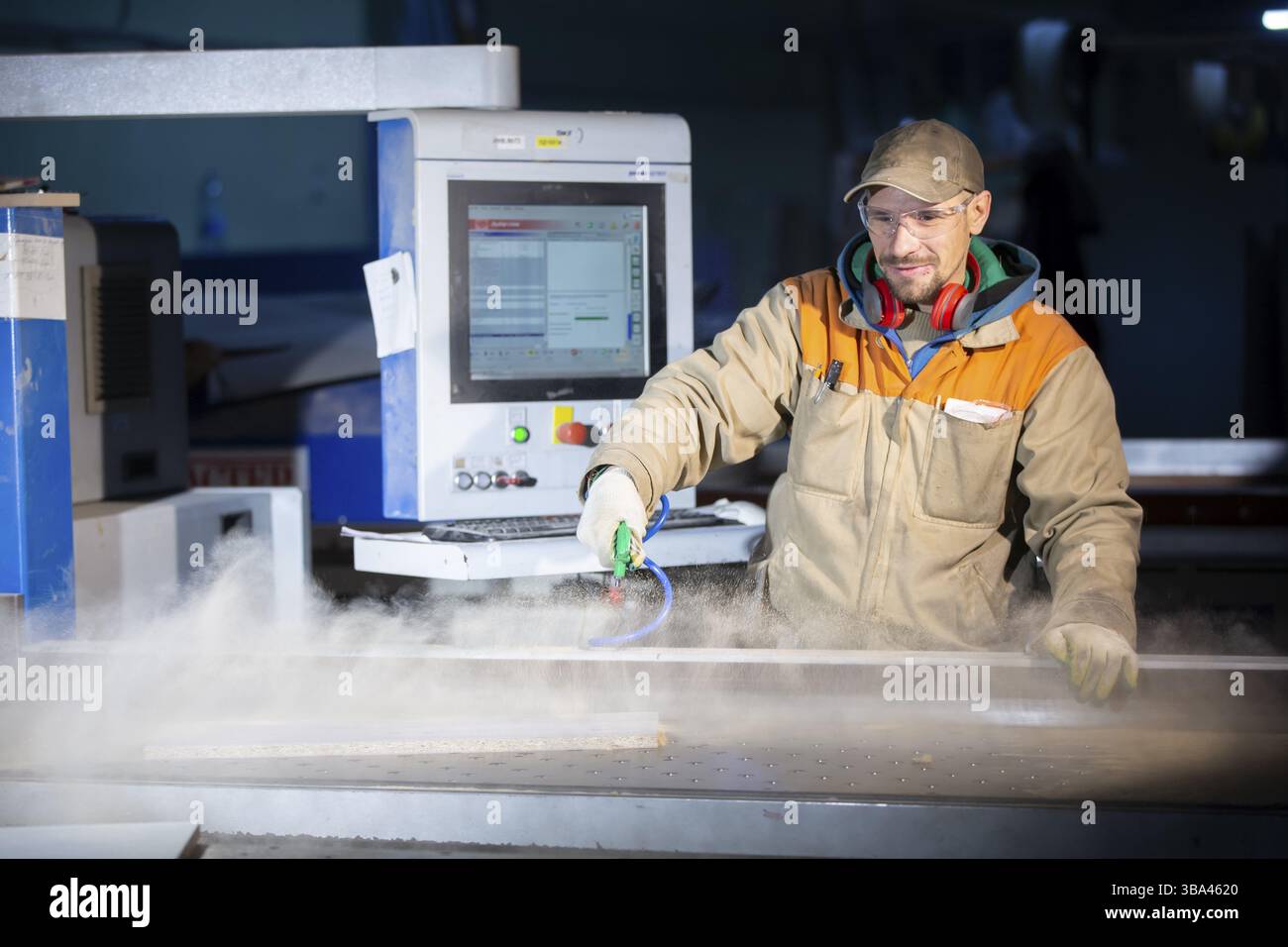 A furniture production worker behind a programmed machine makes furniture parts. Furniture manufacturing Stock Photo