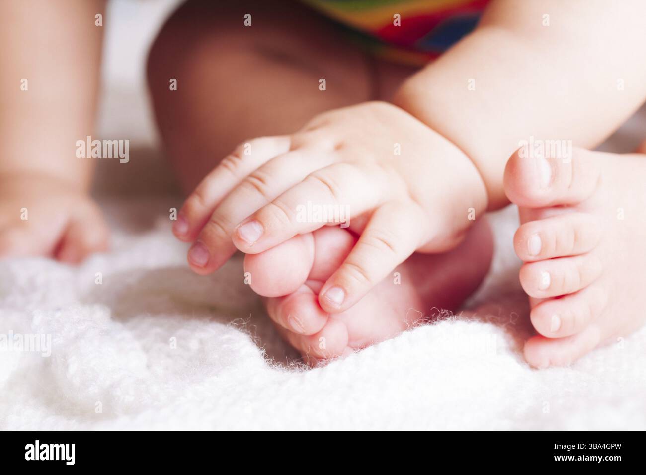 Baby is sitting on the textile. Hands and feet close up Stock Photo