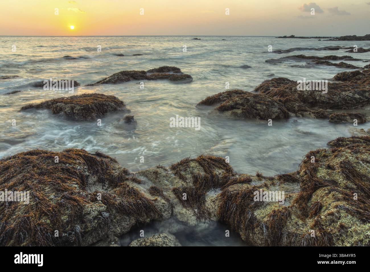 HDR shot of ocean washing the rocks covered with algae and sea weed in susnet light. Koh Lanta, Thailand, Asia Stock Photo