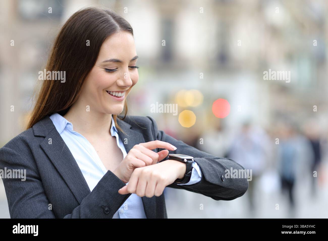 Happy executive standing in the street checking smartwatch Stock Photo