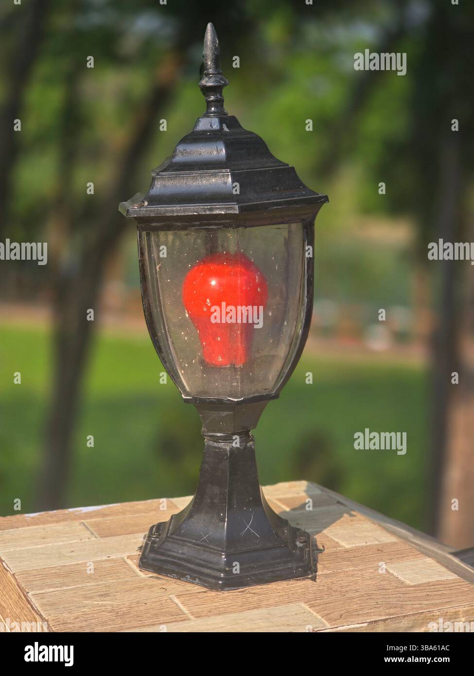 Ornate black outdoor lamp with a glowing red bulb on a textured surface - Smartphone Captured Stock Image