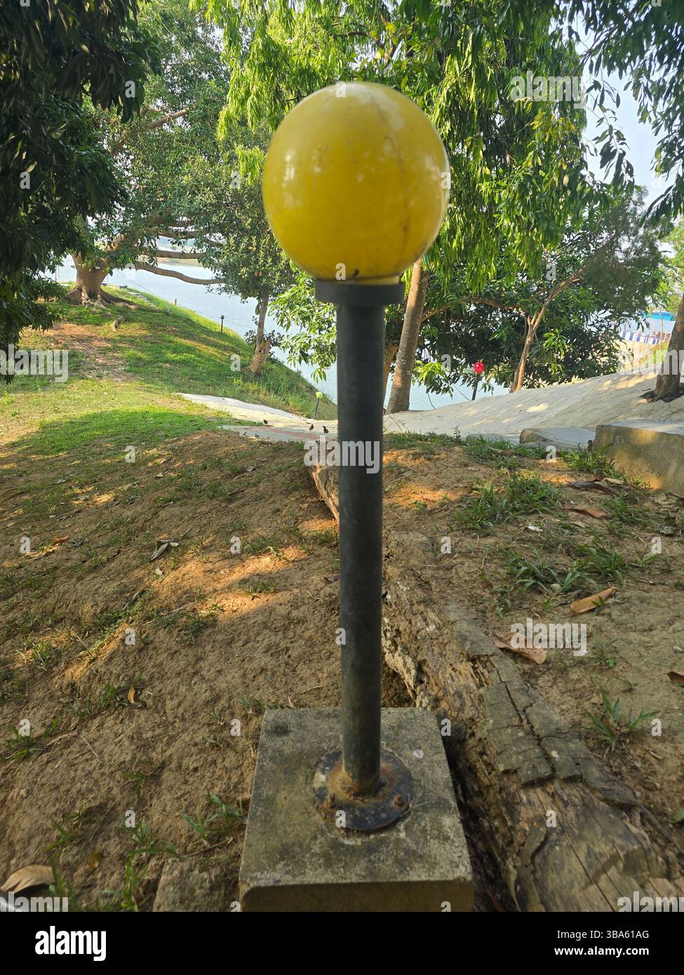 Yellow spherical outdoor lamp on a black pole in a grassy park setting - Smartphone Captured Stock Image