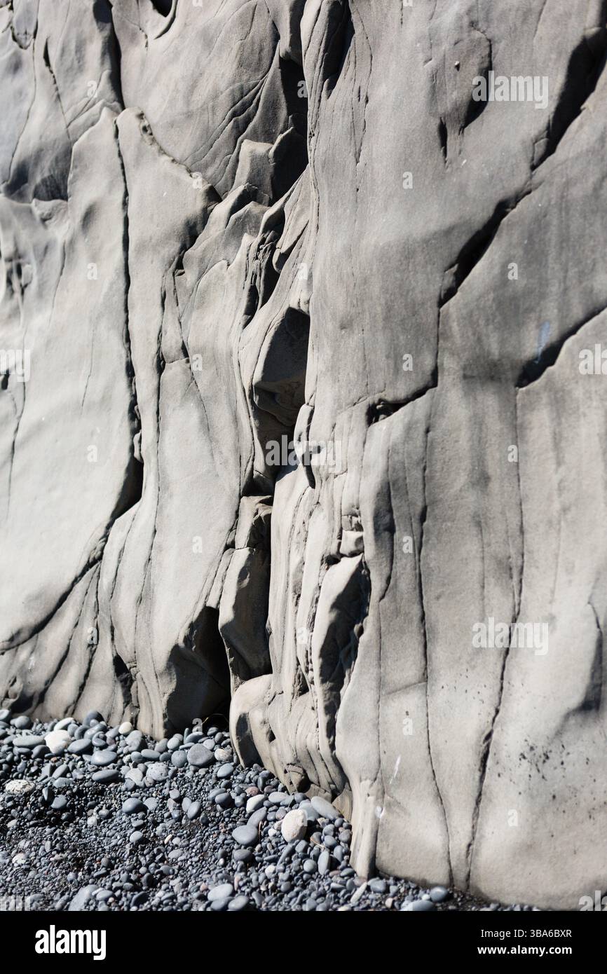 Smooth weathered basalt cliff with dark pebble shore Stock Photo