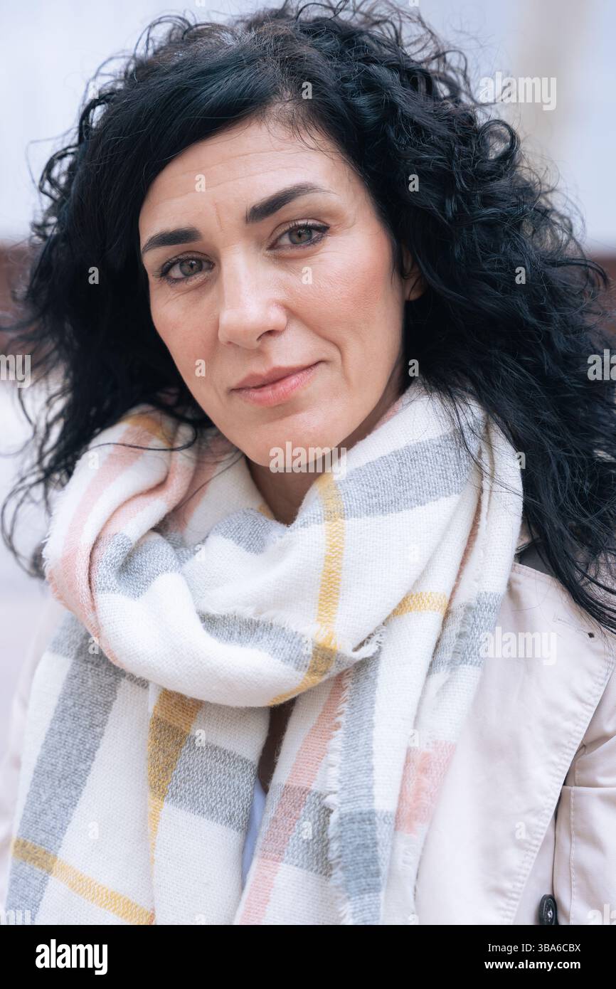 Vertical portrait of woman sitting on bench wearing winter coat and scarf Stock Photo