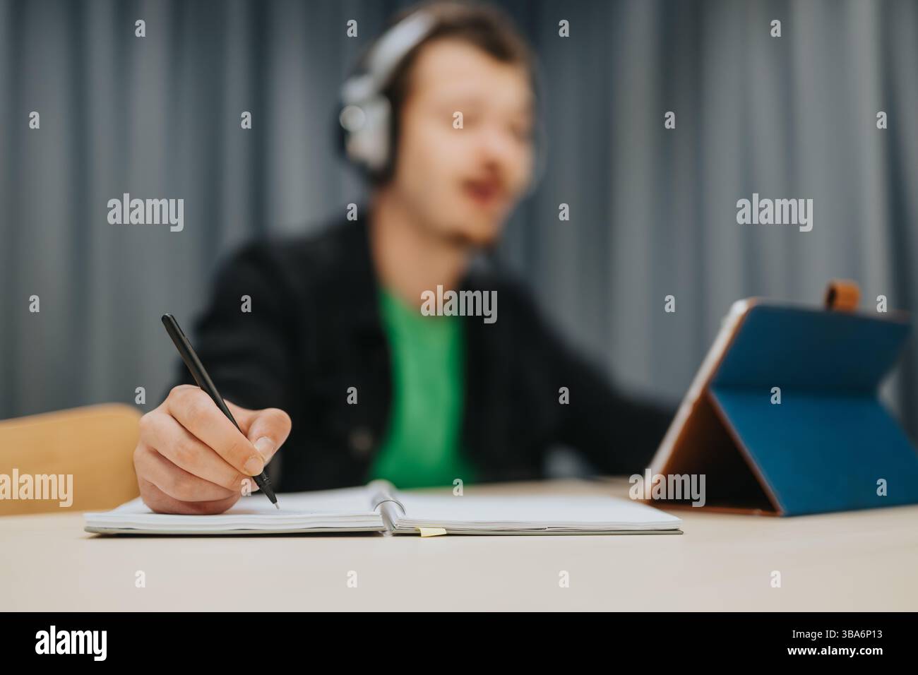 Teenager Studying While Using a Tablet and Taking Notes In a Journal Stock Photo