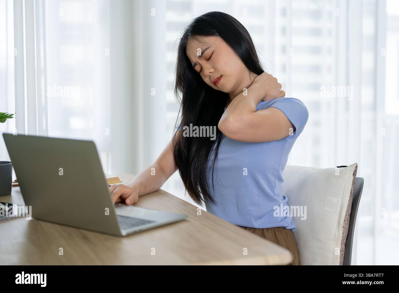 A tired young Asian woman in casual clothes is massaging her neck while ...