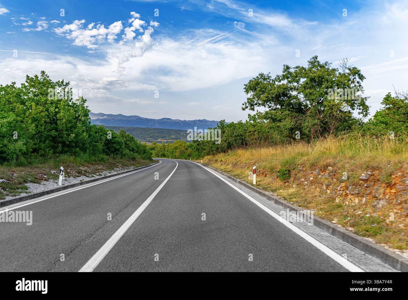 A winding asphalt road curves gently through a green countryside ...