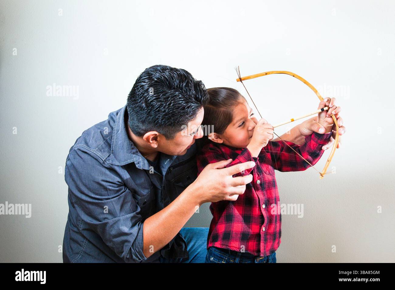 Native American father teaching son how to use toy bow and arrow ...