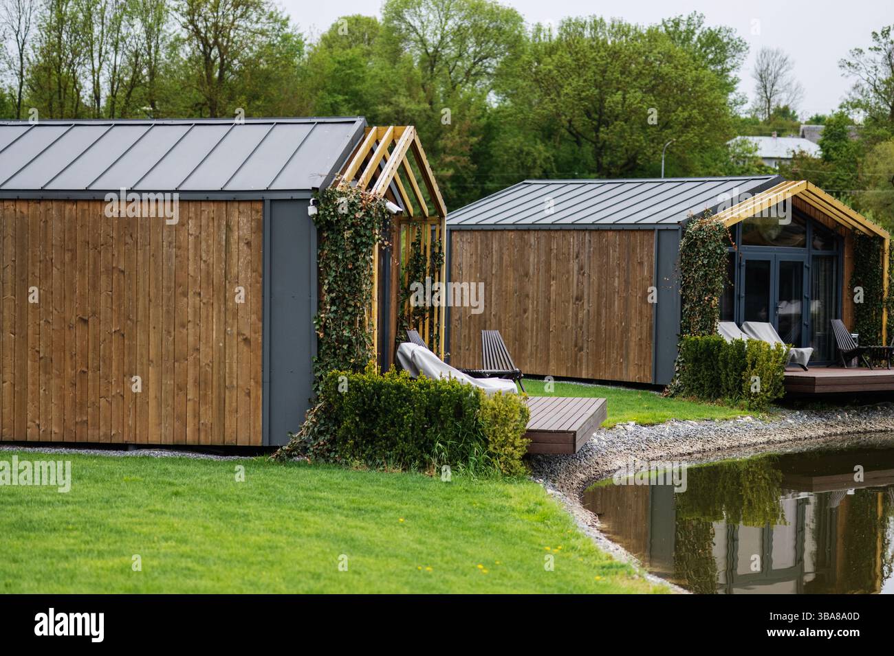 Wooden cabins by a pond surrounded by greenery and trees creating a ...