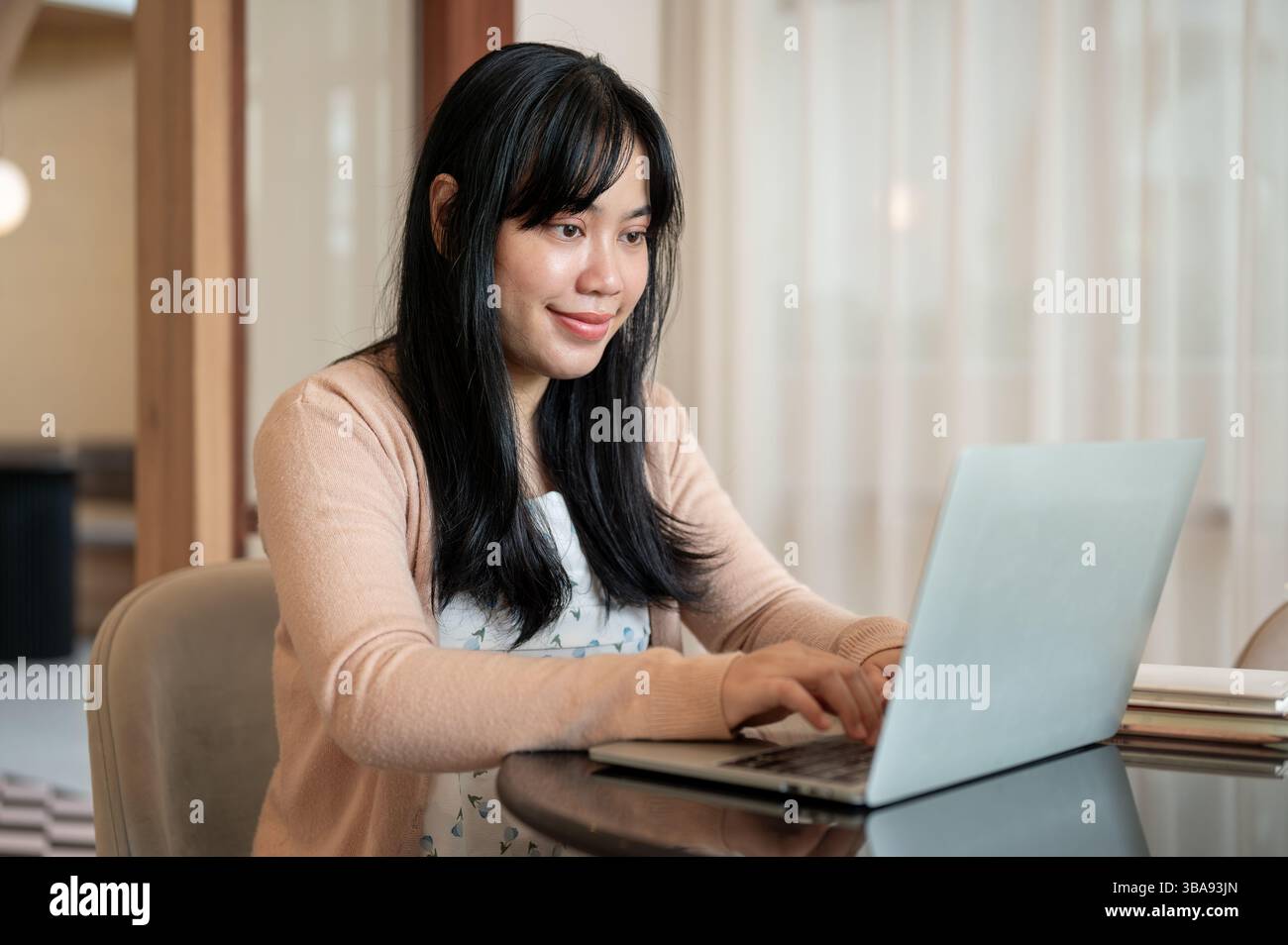 A charming, positive Asian woman is working remotely from a coffee shop ...