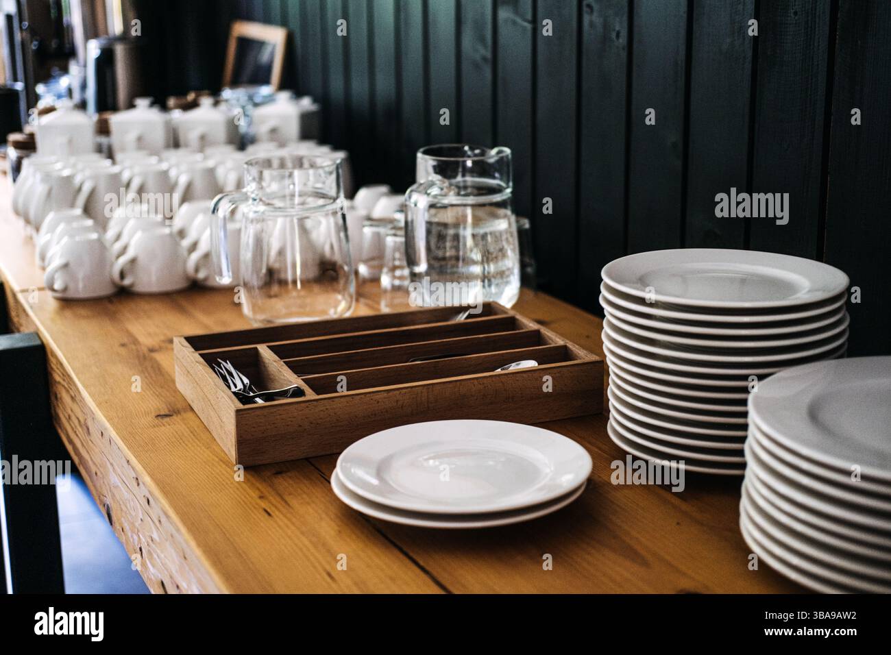 Stacked white plates, mugs, glass pitchers, and cutlery organized ...