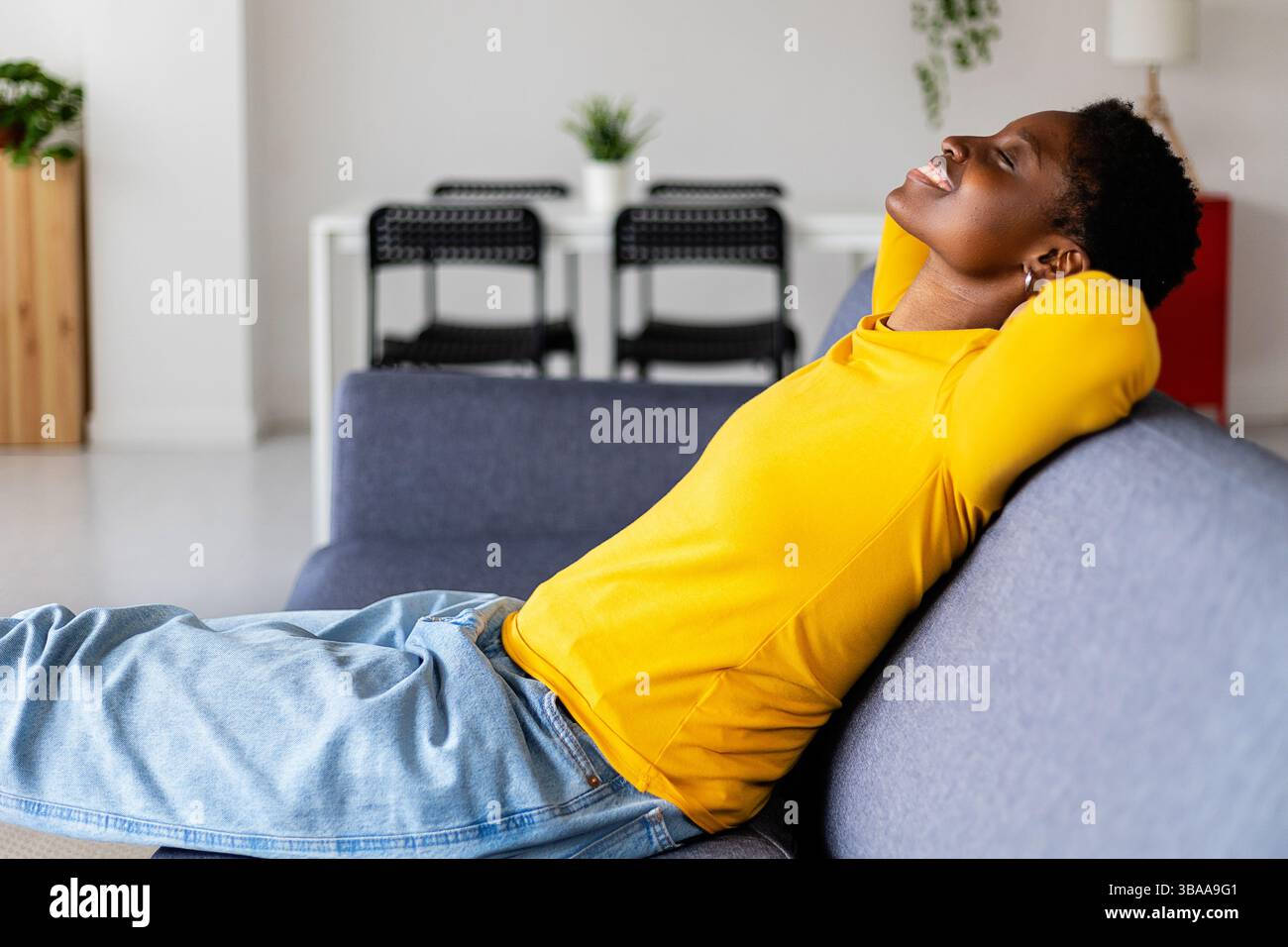 Smiling Black woman with hands behind head and closed eyes sitting and ...